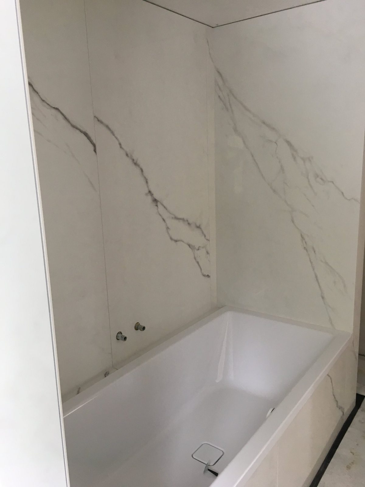 Badewanne vor einer Wand mit weiss-grauer Marmormaserung