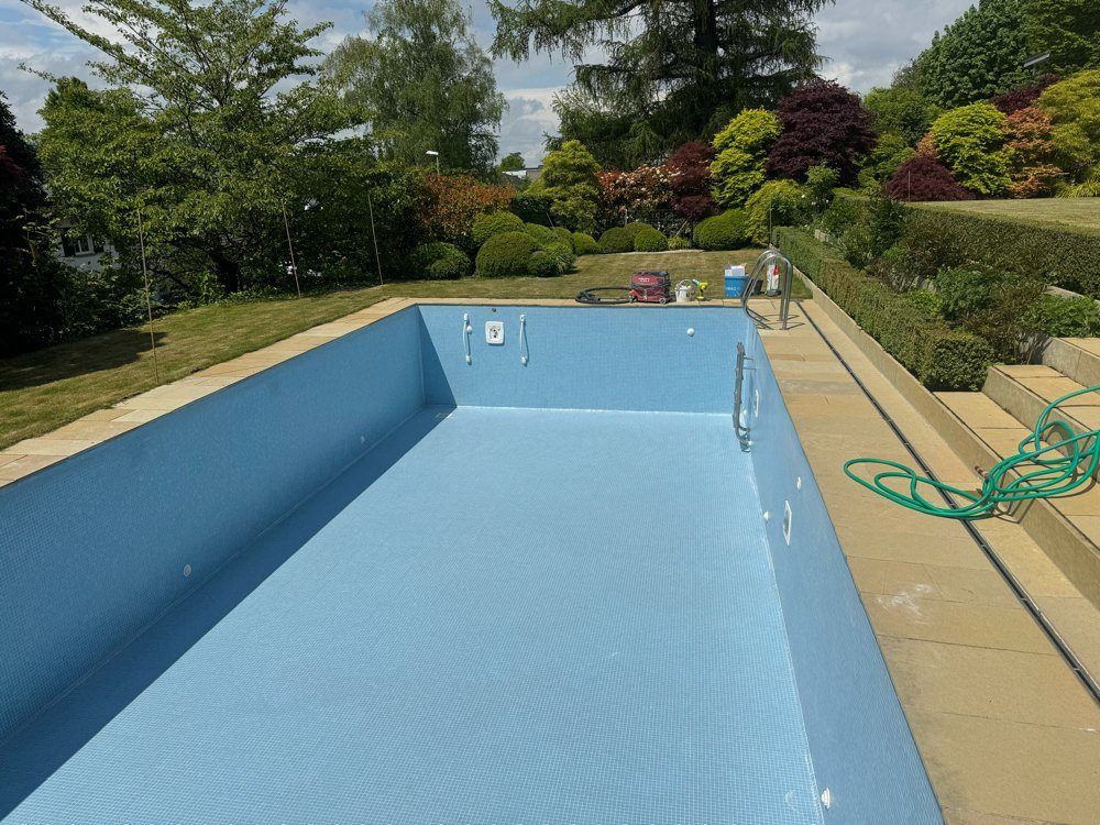 Sanierter Pool mit hellblauem Mosaik in einem Garten